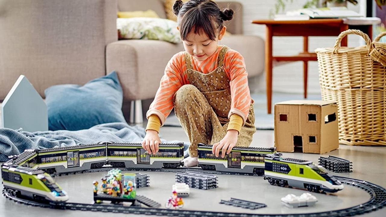 A little girl playing with toy trains on the floor.