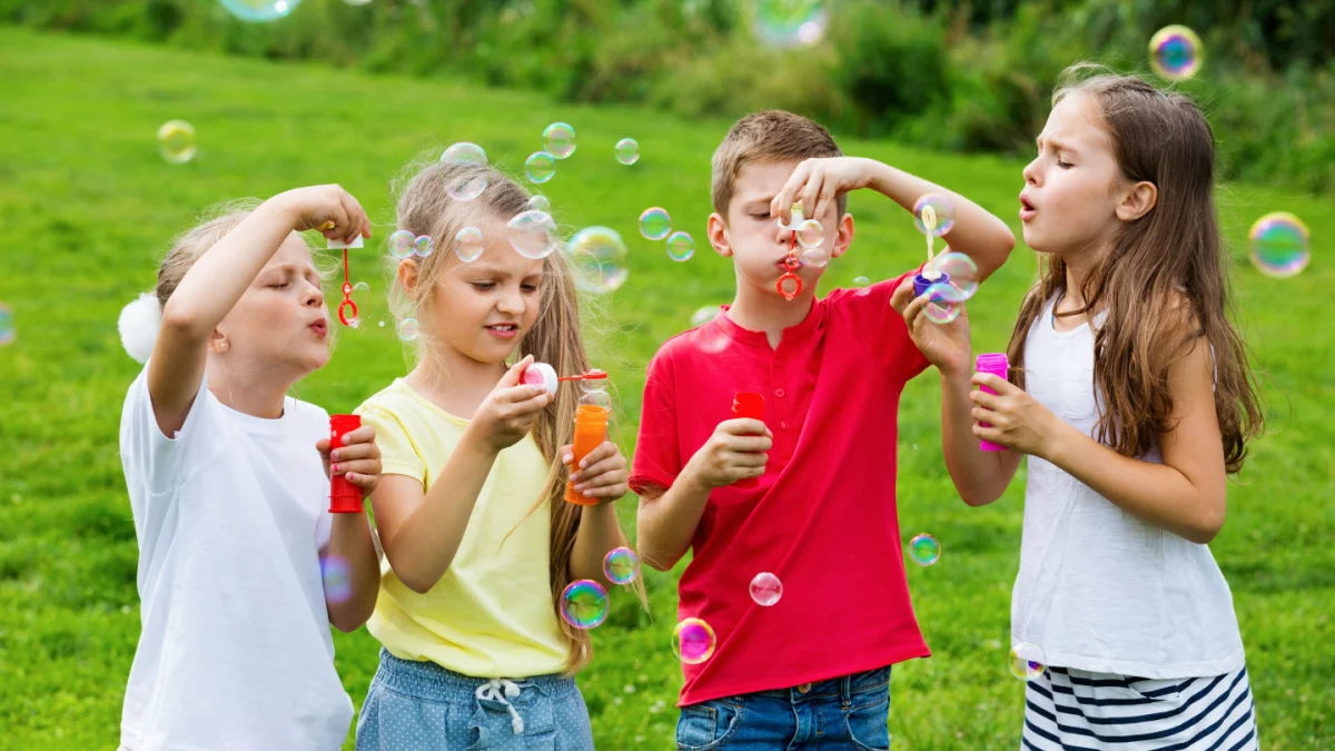 A group of children blowing bubbles in the grass.