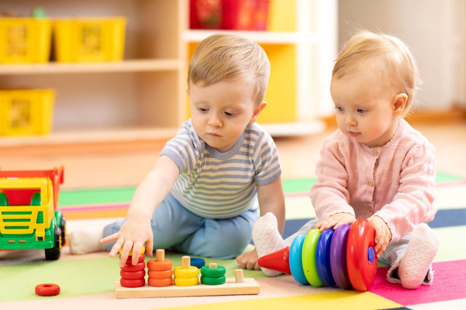 Two babies playing with a toy on the floor.