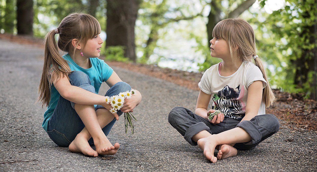 Two children sitting on the ground talking to each other.