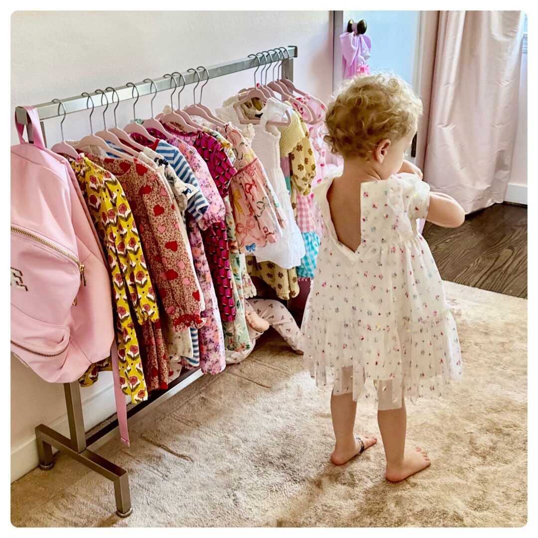 A toddler looking at clothes on a rack.